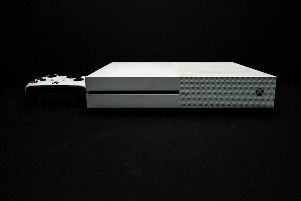 Close-up of a white gaming console with a black controller on a dark background.